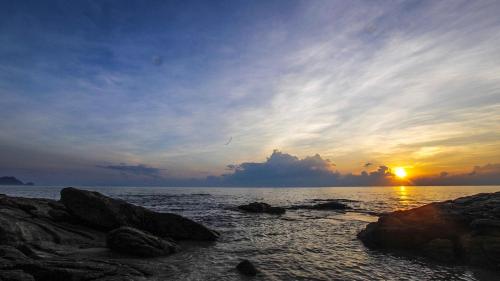a sunset over the ocean with rocks in the water at Khanom Hill Resort in Khanom