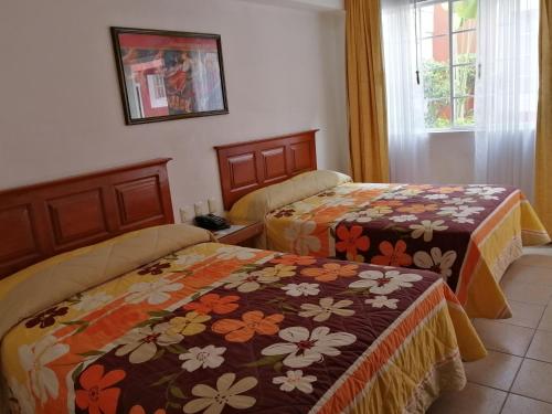 two beds in a hotel room with flowers at Hotel Camba in Oaxaca City
