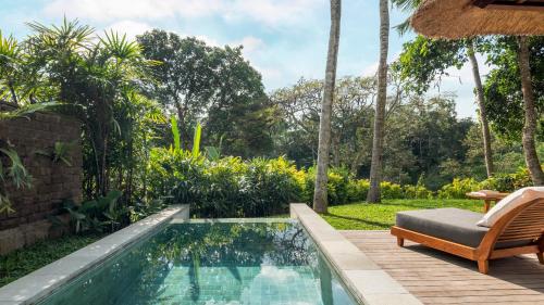 a swimming pool in a garden with a chair and a patio at Maya Ubud Resort & Spa in Ubud