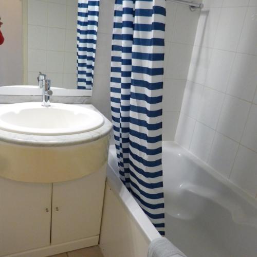 La salle de bains est pourvue d'un lavabo et d'un rideau de douche bleu et blanc. dans l'établissement Les Pins - 3 pièces - Vue sur piscine - 600m mer - Les Sables d'Olonne, à Les Sables-dʼOlonne