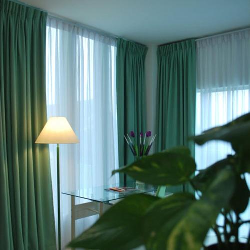a room with green curtains and a table with a plant at MCITI Suites in Miri