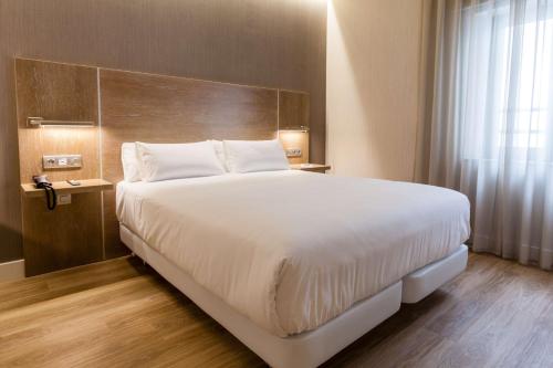 a bedroom with a large white bed with a wooden headboard at NH Oviedo Principado in Oviedo