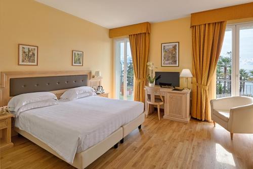 a bedroom with a bed, chair, desk and a television at Hotel Paradiso in Sanremo