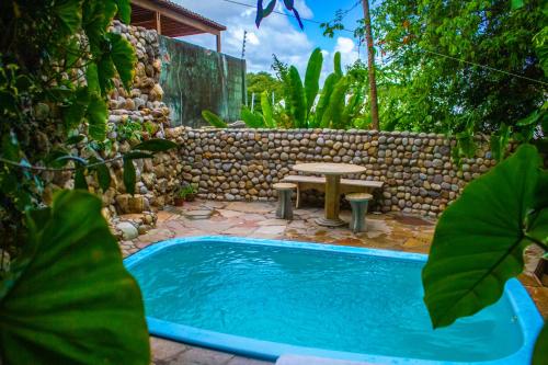 a pool with a picnic table and a stone wall at Refúgio das Fadas in Pipa