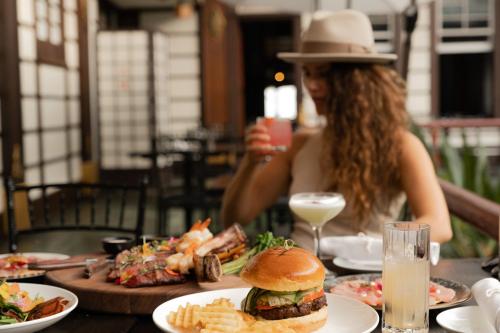 a woman sitting at a table with a hamburger and french fries at Hollywood Hills Hotel in Los Angeles
