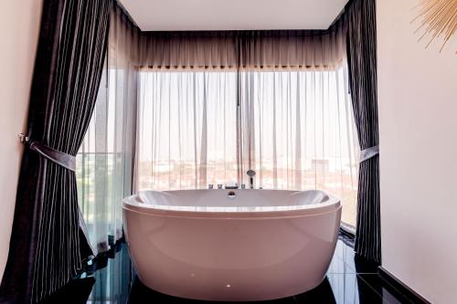 a bathroom with a tub in front of a large window at The Proud Hotel Pattaya - SHA Certified in Pattaya North