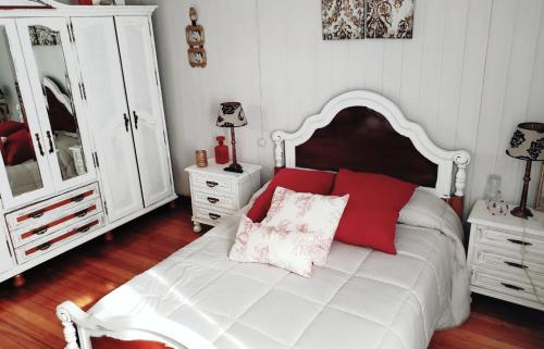 1 dormitorio con cama blanca y almohadas rojas en Casa de piedra en Costa da Morte., en A Ponte do Porto