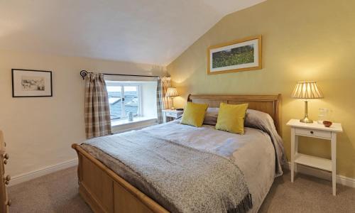 a bedroom with a bed with yellow pillows and a window at Smithy Cottage At Lindeth in Windermere
