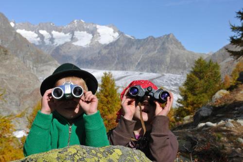 two people looking through binoculars with mountains in the background at Bettmerlodge in Bettmeralp