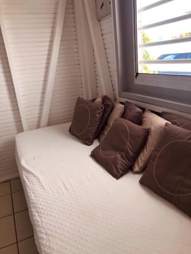 a couch with pillows sitting next to a window at TI-MANGO 1km de la plage communale quartier résidentiel in Sainte-Anne