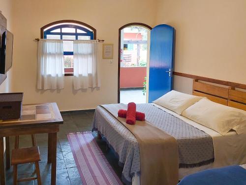1 dormitorio con 1 cama, 1 mesa y 2 ventanas en Sollar dos Gerânios, en Peruíbe