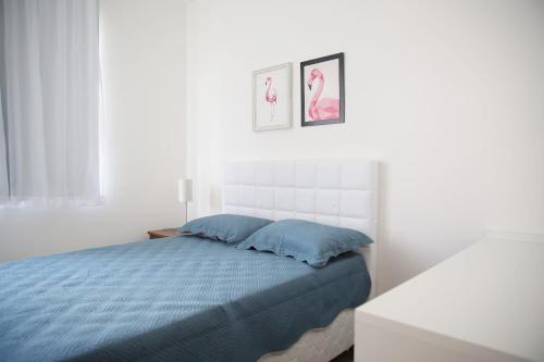 a white bedroom with a blue bed with two pictures on the wall at Apartamento Premium in Diamantina