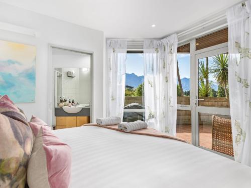 a bedroom with a large white bed and a balcony at Maison de Charme Central Apartment in Queenstown
