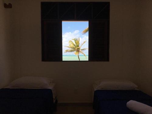 a window in a room with two beds and a palm tree at Morada dos Cataventos (Frente Mar) in Barra de Camaratuba