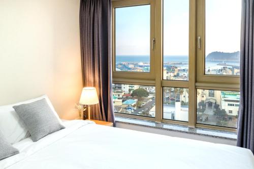 a bedroom with a white bed and large windows at Shin Shin Hotel Seogwipo in Seogwipo