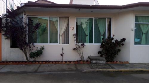 a white house with green curtains on the windows at Villa kosniin in Tecolutla
