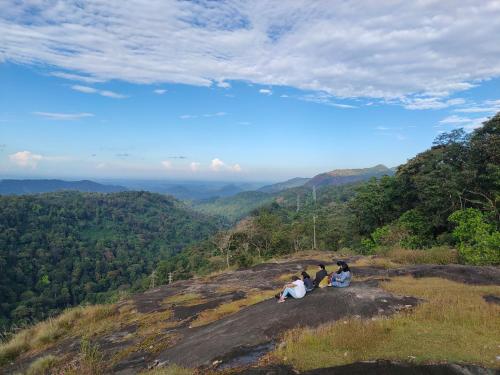 three people sitting on the edge of a mountain at Beyond Eco Living in Munnar