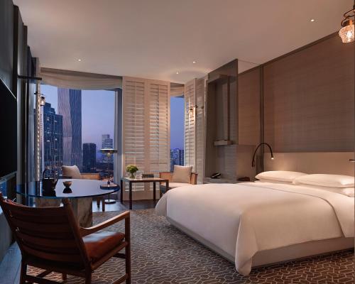 a bedroom with a bed and a desk and a room with a view at Andaz Shenzhen Bay in Shenzhen