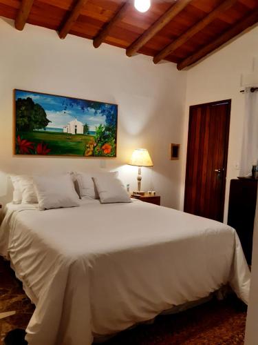 a bedroom with a white bed with a painting on the wall at Casa Rabanete Trancoso in Trancoso