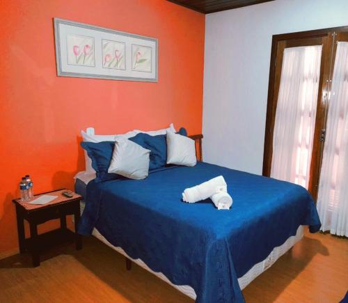 1 dormitorio con cama azul y pared de color naranja en Pousada Monte Suiço, en Campos do Jordão