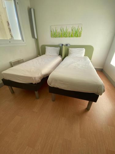two twin beds in a room with wood floors at ibis Budget Caen Centre Gare in Caen
