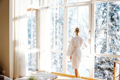 a woman in a white robe looking out of a window at Hotel Annelies in Ramsau am Dachstein
