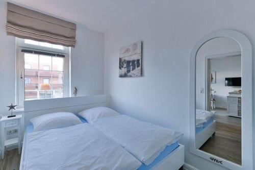 a white bedroom with a bed and a mirror at App-8-in-strandnaher-Lage-Baederstil-Villa-in-Wenningstedt-Sylt in Wenningstedt