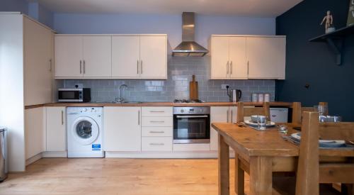 a kitchen with white cabinets and a wooden table at Lovely Coach House with Free Parking in Cardiff