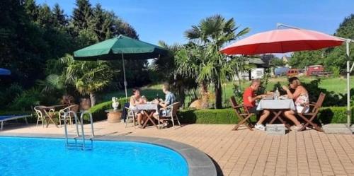 a group of people sitting at tables with umbrellas near a pool at B&B Casa Roman & Vakantiewoning voor 1 pers tot max 32 personen in Zonhoven