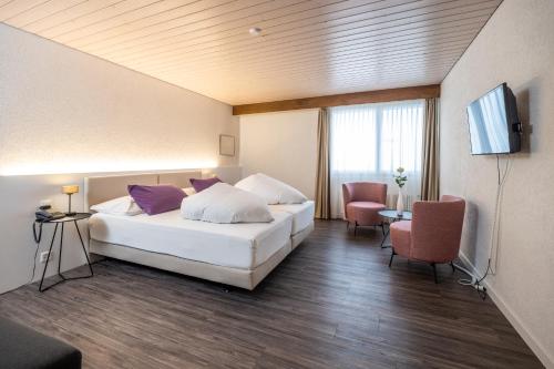 a bedroom with a bed and two chairs and a television at Hotel Rischli in Sörenberg