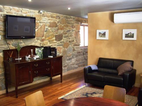 a living room with a couch and a tv on a stone wall at 1860 Wine Country Cottages in Springton