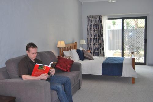 a man sitting on a couch reading a book at Brayfield Cottage in Murray Bridge