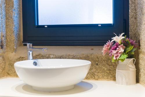 a bathroom with a white sink and a vase of flowers at Carrioza Alojamiento Turístico in Parada del Sil