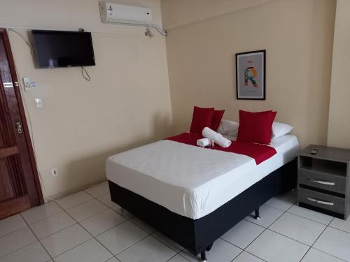 a bedroom with a bed with red pillows and a tv at Hotel PS Itaboraí in Itaboraí