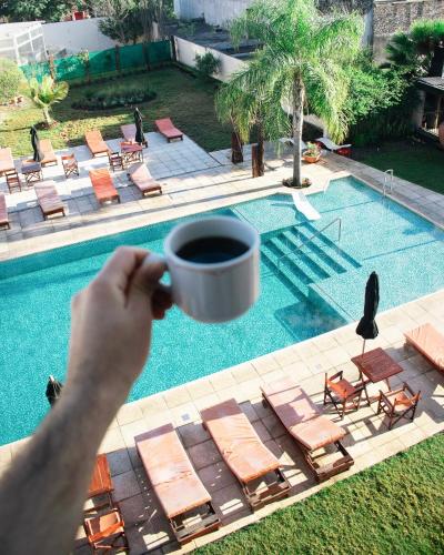 a person holding a cup of coffee next to a pool at Hotel Termal Los Cardones & Spa in Termas de Río Hondo