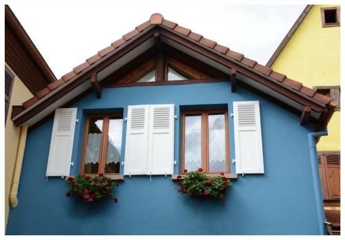 Gîte La Maison Bleue في برغهايم: منزل أزرق عليه نوافذ وزهور