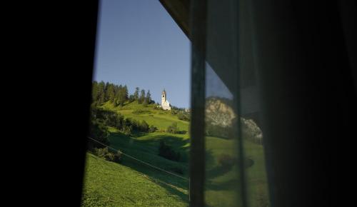 a window with a view of a green hill with a church at Lüch de Crusteles in La Valle