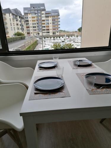 une table blanche avec des assiettes et des verres ainsi qu'une fenêtre dans l'établissement Les Marines, à Courseulles-sur-Mer