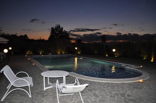 uma mesa e cadeiras ao lado de uma piscina à noite em La Tenuta del Barone em SantʼAgata deʼ Goti