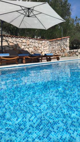 a swimming pool with an umbrella and chairs and a swimming pool at Stone hause Noa in Rab