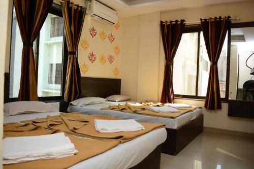 two beds in a room with windows and curtains at Hotel Sai Sampada NX in Shirdi