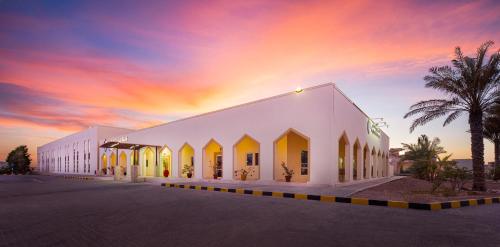 a large white building with a sunset in the background at City Hotel Duqm in Duqm