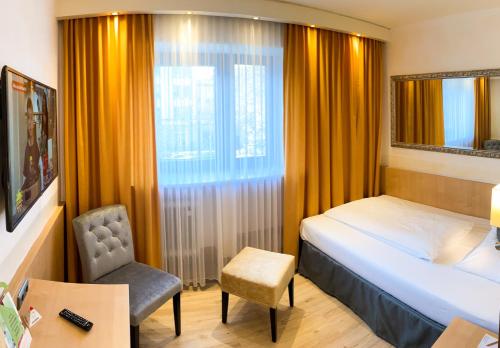 a bedroom with a bed and a chair and a window at City Hotel Ost am Kö in Augsburg
