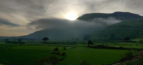 a sun setting over a green field with a mountain at Nivaant, at Igatpuri in Igatpuri