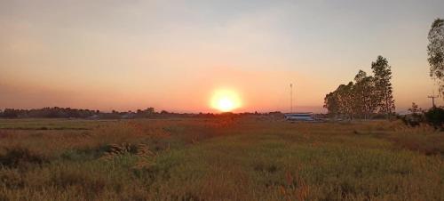 a sunset in a field with the sun setting at บ้านนอกเมืองรีสอร์ต BaanNokMueang in Phayao