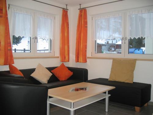 サースフェーにあるHoliday Home Haus Alpenstern- Wohnung Aelpi by Interhomeのリビングルーム(黒いソファ、オレンジ色のカーテン付)