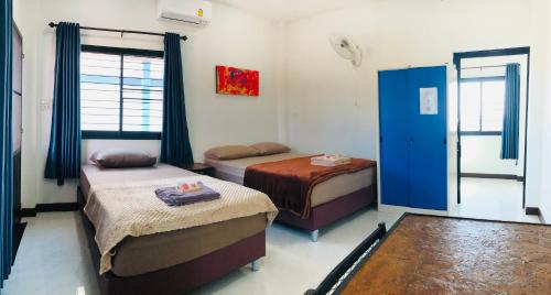 a bedroom with two beds and a blue door at บ้านนอกเมืองรีสอร์ต BaanNokMueang in Phayao