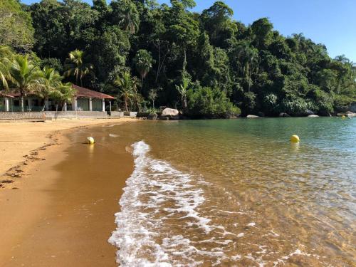 a beach with a shoreline with trees in the background at Pousada Vitorino in Angra dos Reis