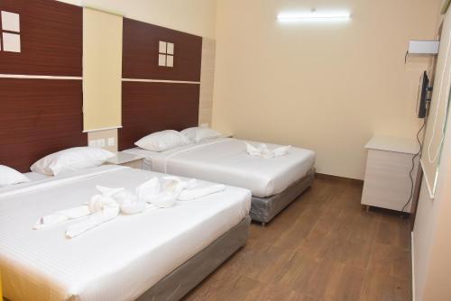 two beds in a hotel room with white sheets at Murali's Kudil in Mayiladuthurai