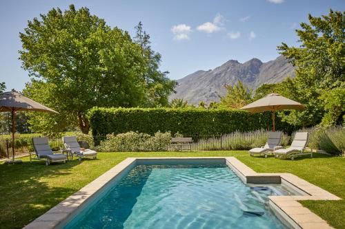 a swimming pool in a yard with chairs and umbrellas at La Clé Lodge in Franschhoek
